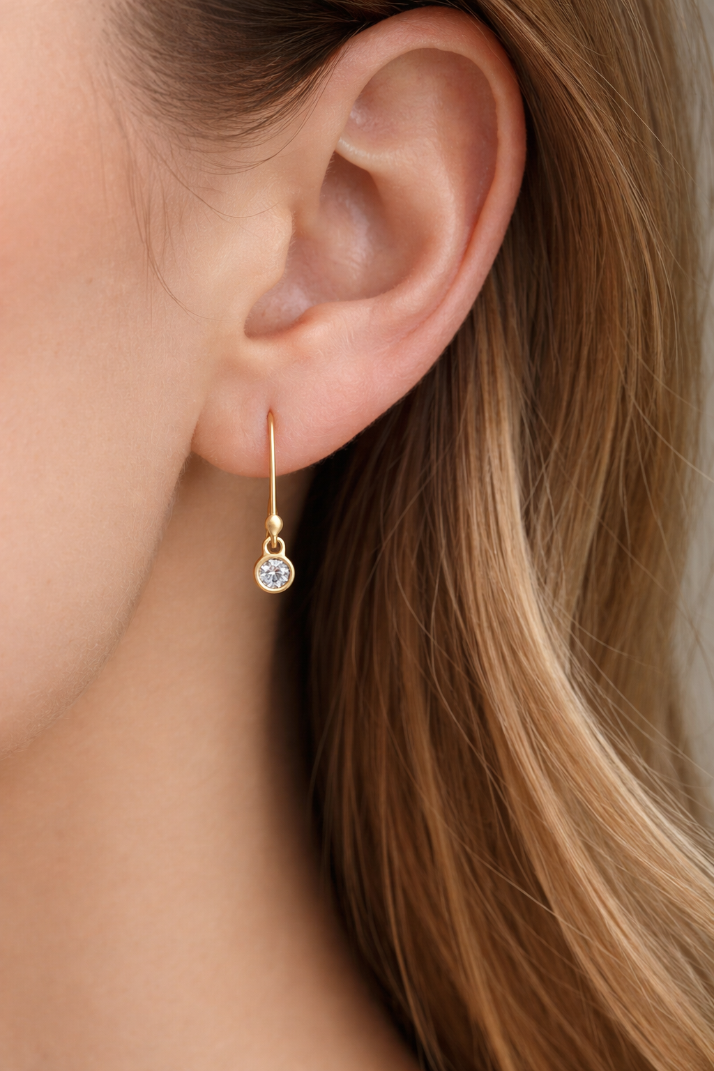 Close-up of an ear wearing a gold earring with a gemstone.
