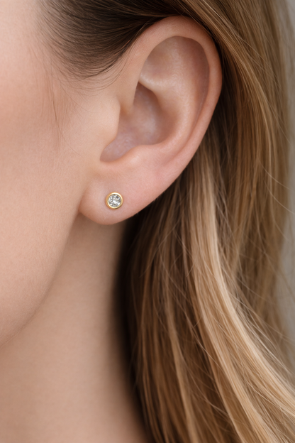 Close-up of an ear wearing a gold earring with a clear gemstone.
